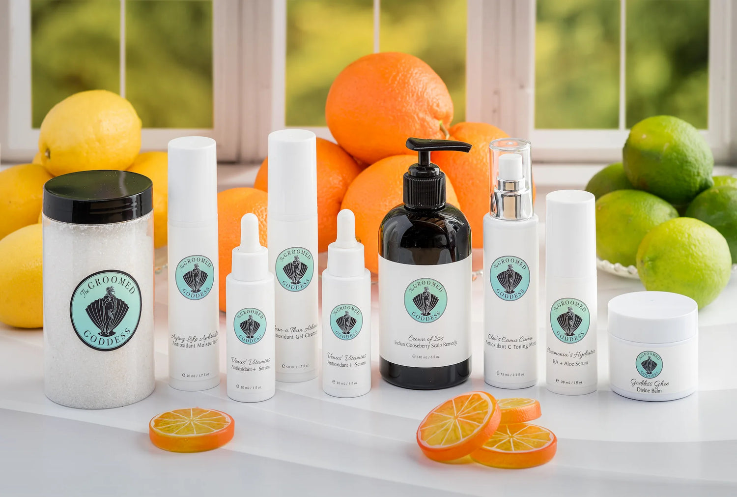 Collection of The Groomed Goddess skincare products with citrus fruits on a white surface