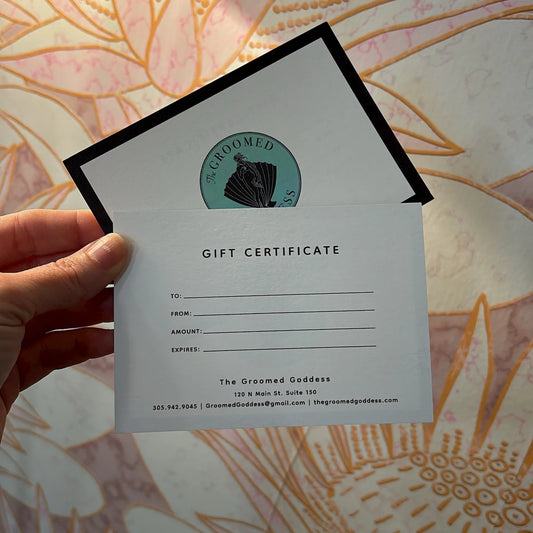A Groomed Goddess Gift certificate held by a hand with a decorative background